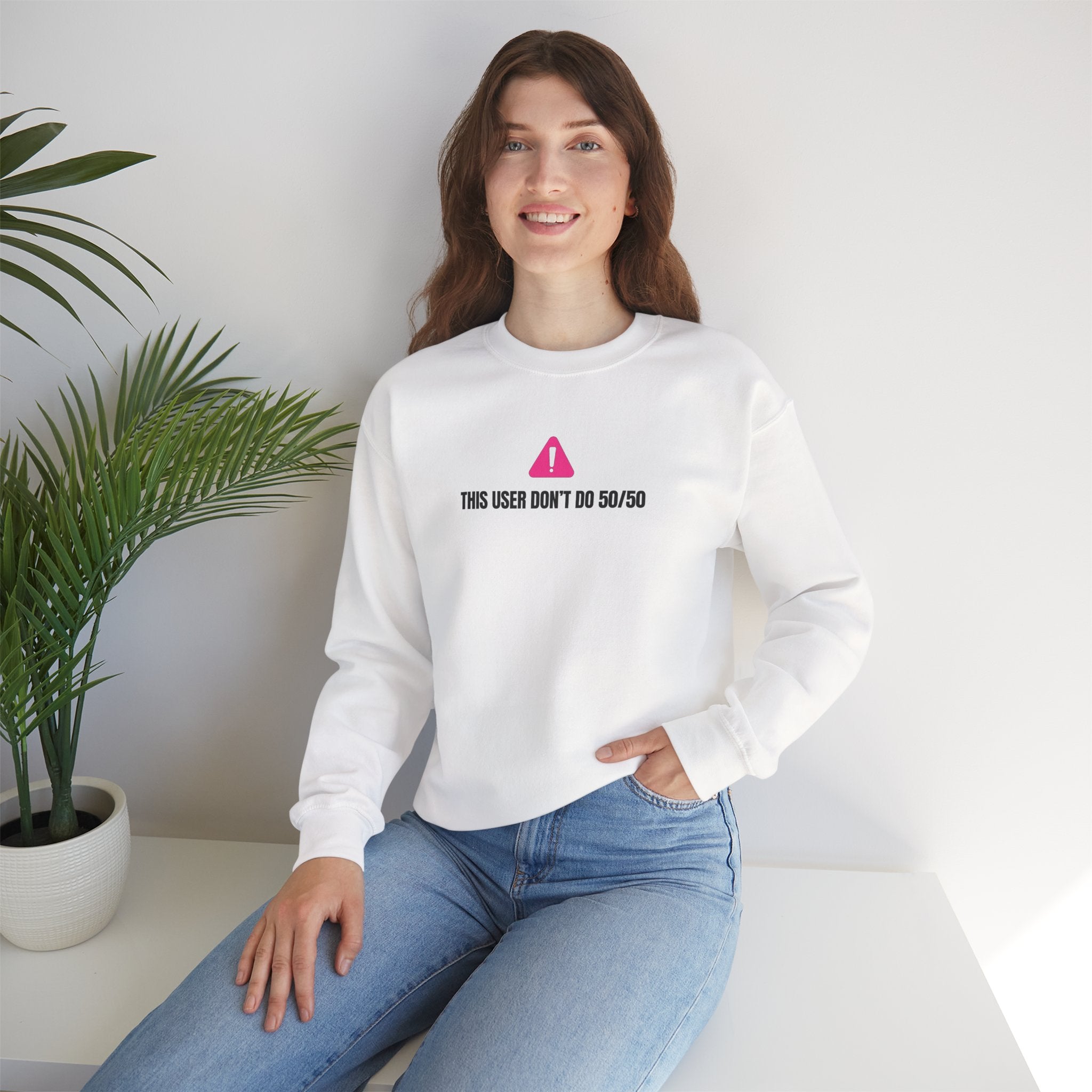 This user don’t do 50/50 sweatshirt - Person wearing a white sweatshirt with a logo and text, sitting in a room with a plant.